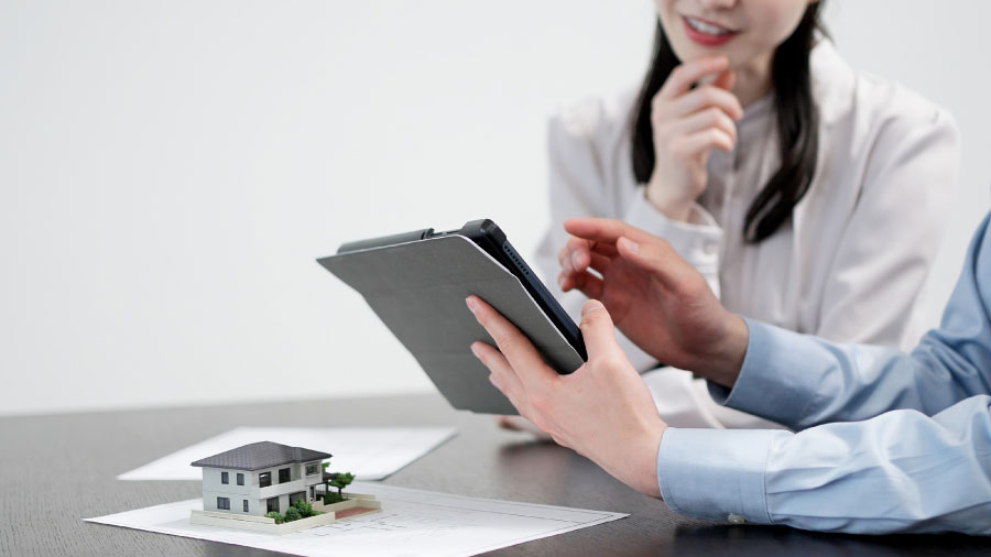 一戸建ての模型が置かれたテーブルで不動産業者の説明を受ける人