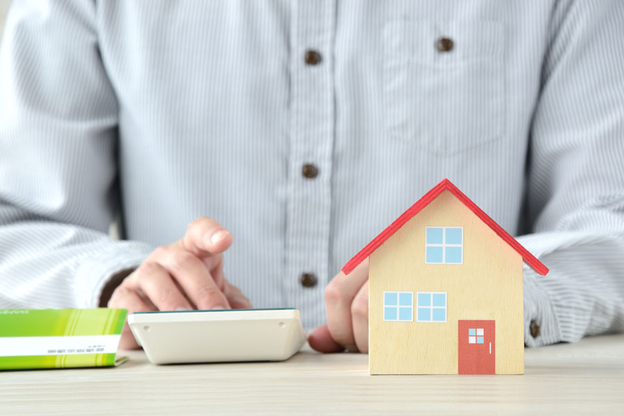テーブルの上に置かれた小さな家の模型と電卓を使い、計算している男性