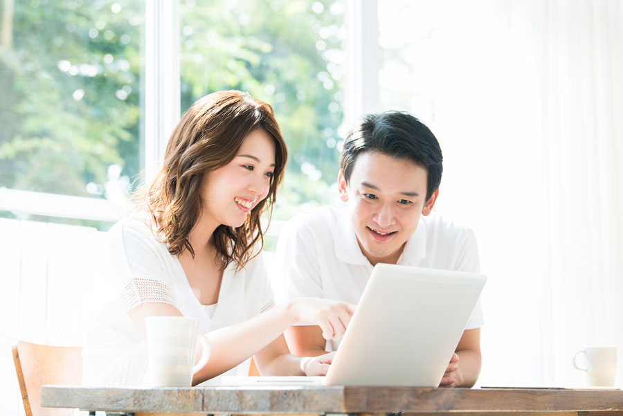 明るい部屋で、若い男女がノートパソコンを見ながら笑顔で話している様子