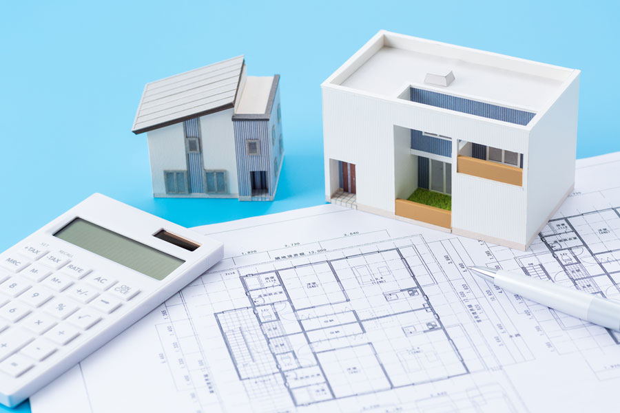 設計図の上に置かれた住宅の模型とペン、電卓