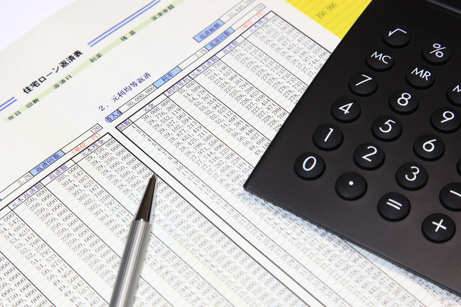 住宅ローン返済表の上に置かれたボールペンと電卓
