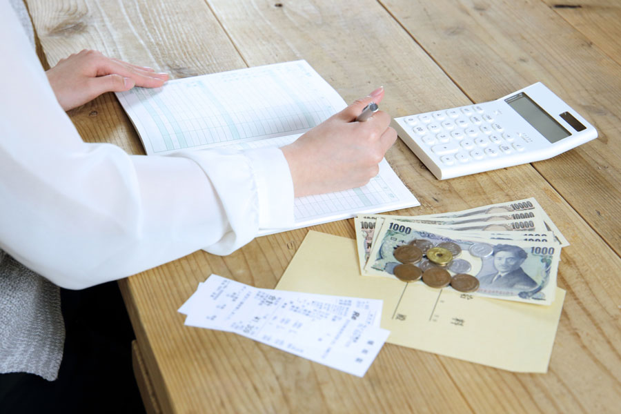 机にお金と電卓を置いて計算する人の手元