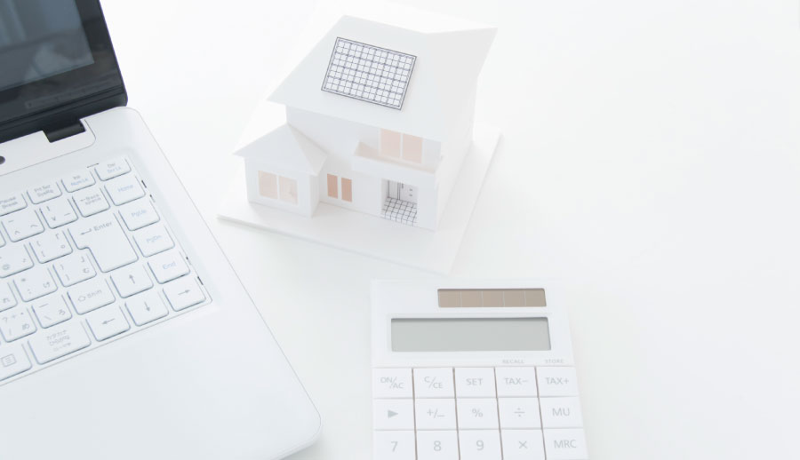 デスクに置かれた住宅の模型と電卓・ノートパソコン