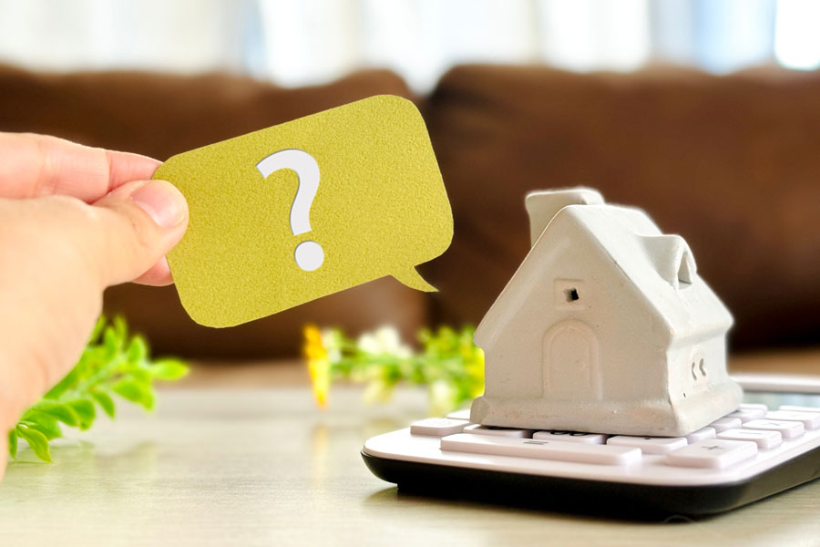 電卓の上に置かれた住宅の模型とクエスチョンマークのステッカーを持つ手