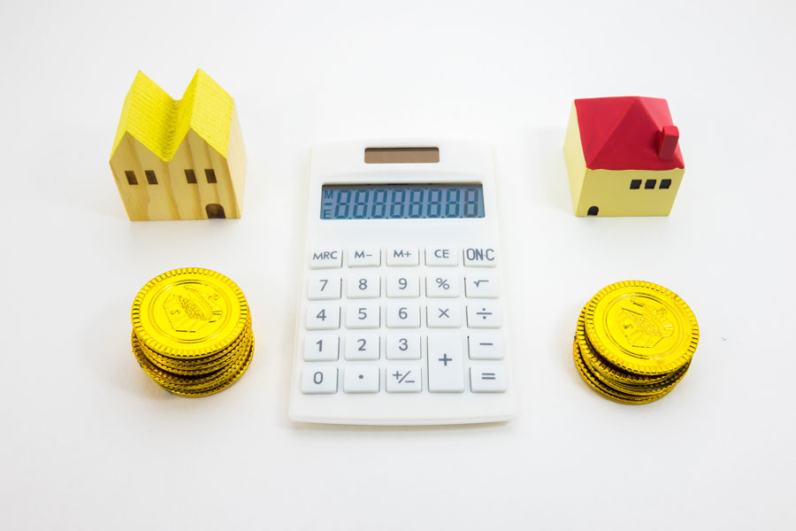 2つの家の模型と電卓、金色のコインが並んでいる