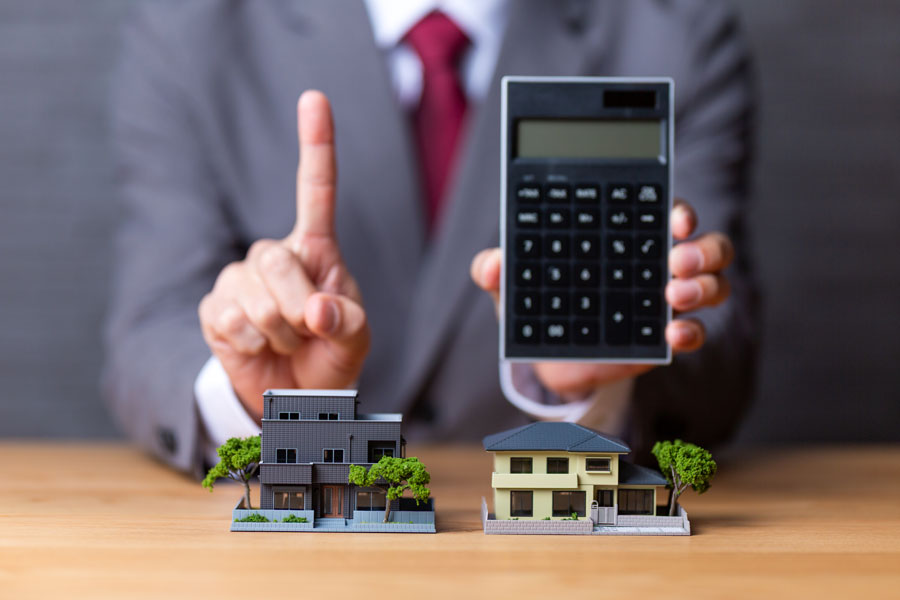 住宅模型と電卓と人差し指を立てるスーツ姿の男性
