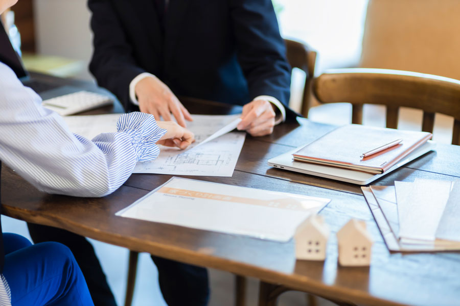 新築住宅の打ち合わせをする男女。テーブルには図面や書類、住宅模型が並んでいる