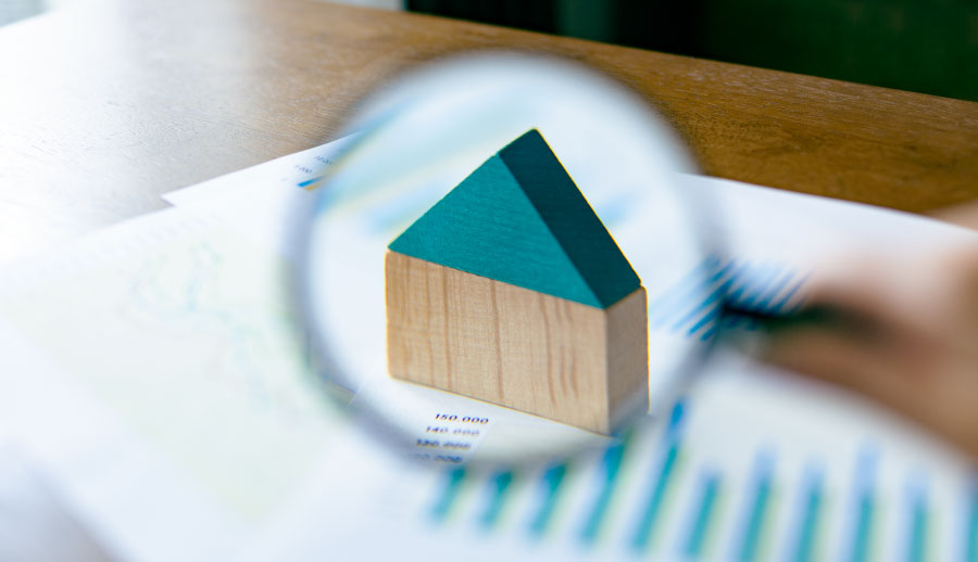 書類の上に置かれた木製の家の模型を、虫眼鏡で拡大している様子