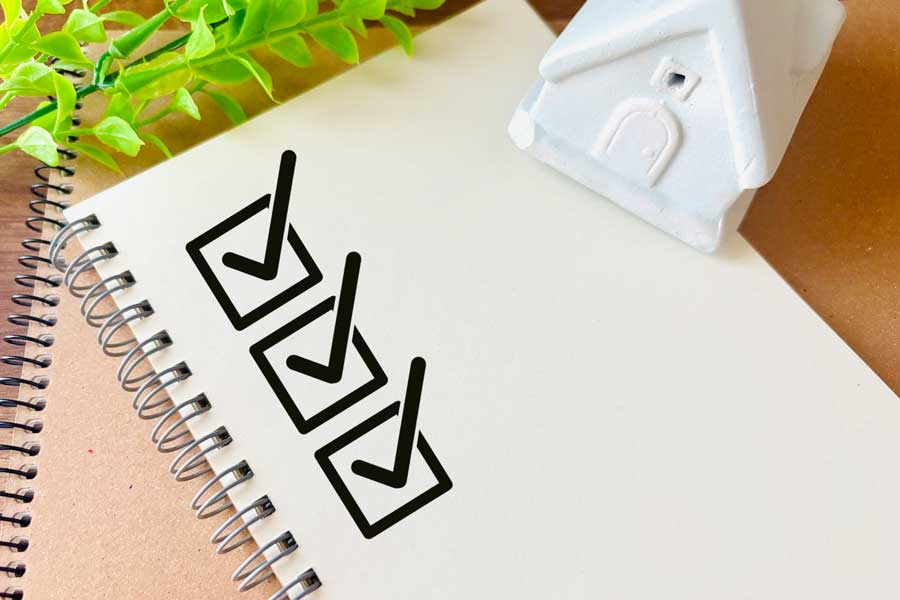 チェックリストが書かれたノートと白い住宅の模型