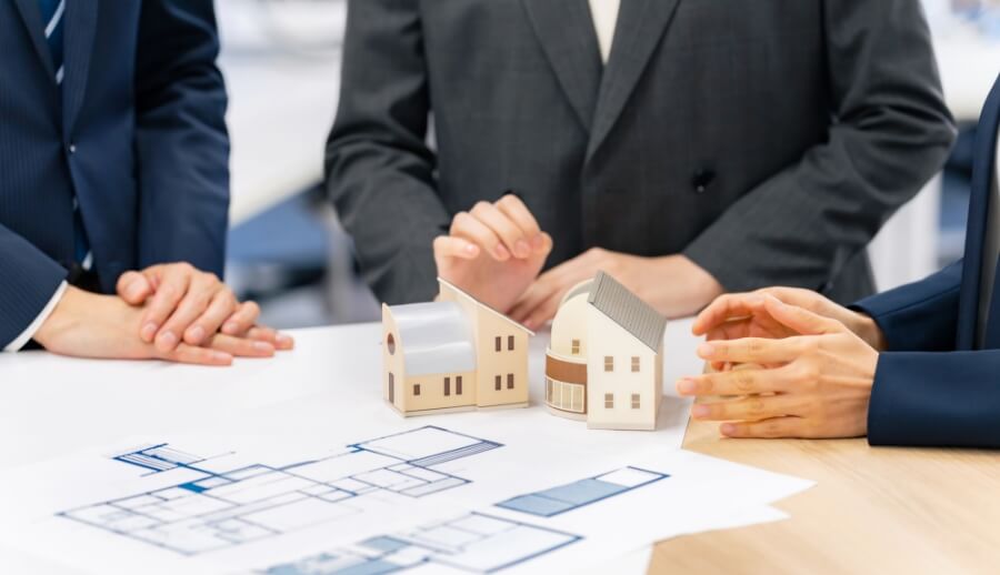 住宅の模型と設計図を囲んで相談するビジネスパーソンたち