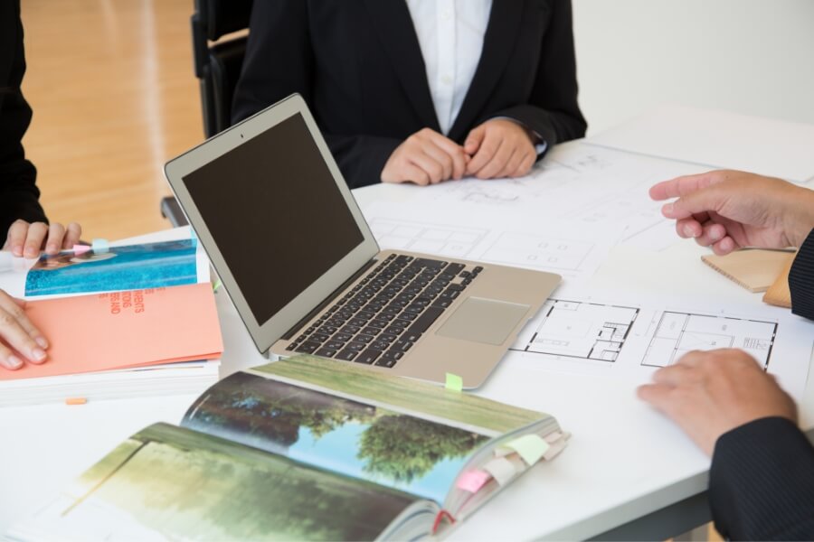 カタログとノートパソコン・設計図を見ながら住宅について相談する人々